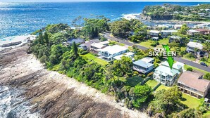 An aerial view of a coastal residential area with houses, greenery, and a beach.