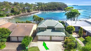 A coastal house with a garage, surrounded by lush greenery and a view of the ocean.