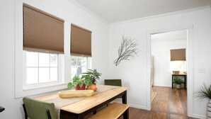 A dining area with a wooden table, two chairs, and a bench. There are two windows with blinds, a potted plant, and a wall-mounted branch decoration. - 2 BR/1BA / IMMACULATE/ DOWNTOWN.
 HIIKE THE CANYON.
PETS WELCOME with SMALL FEE. (Canyon)