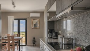 A modern kitchen with granite countertops, a built-in stove, and a dining area with a view. - Queen Bee Residence- Queen Apartment (Minia, Kefalonia)