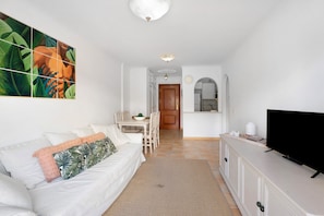 A living room with a white sofa, a flat-screen TV, a dining area with a table and chairs, and a kitchen area with cabinets and a countertop. - Holiday Home "Our Home" with Shared Pool, Terrace & Wi-Fi (Arona)