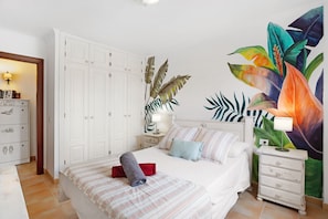 A bedroom with a bed, a nightstand, a dresser, and a wall with a tropical mural. - Holiday Home "Our Home" with Shared Pool, Terrace & Wi-Fi (Arona)