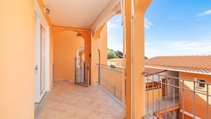 A corridor with a tiled floor, a metal railing, and a door leading to a balcony.
