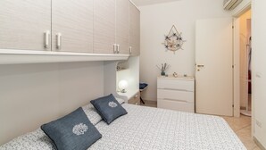 A bedroom with a bed, a dresser, a vanity with a mirror, and a wall-mounted air conditioner.