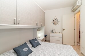 A bedroom with a bed, a dresser, a vanity with a mirror, and a wall-mounted air conditioner.