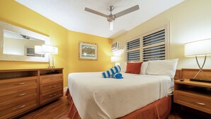 Une chambre d’hôtel avec un lit, une commode en bois, un ventilateur de plafond et un tableau au mur.