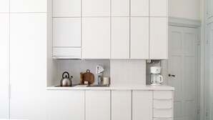 Una cocina moderna con armarios blancos, un hervidor, una cafetera y una tabla de cortar de madera.