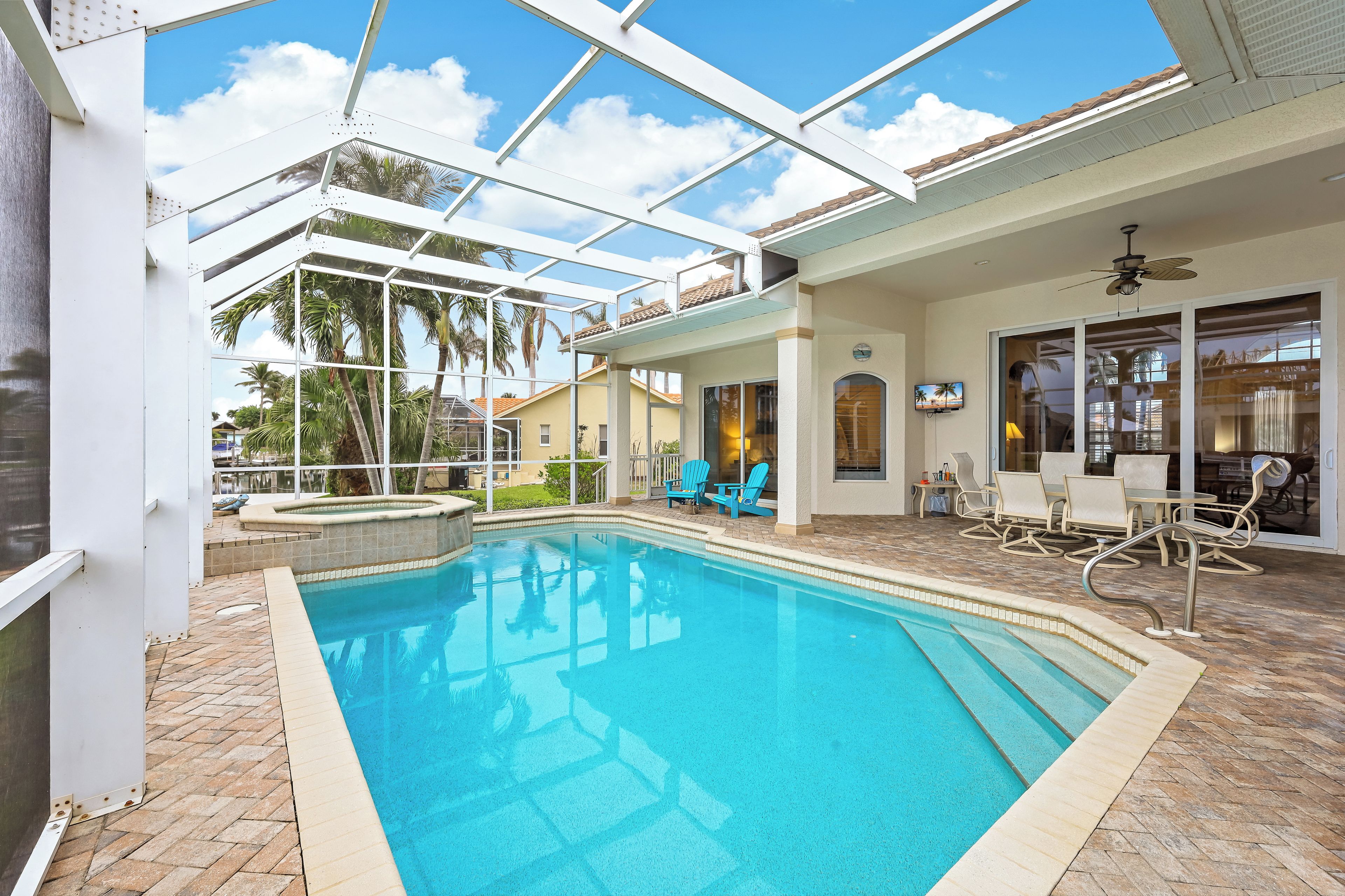 A pool area with a glass ceiling, outdoor seating, and a view of palm trees.