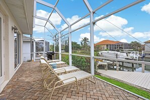 Eine überdachte Terrasse mit Liegestühlen, ein Ziegelboden und Blick auf einen Yachthafen mit Booten.