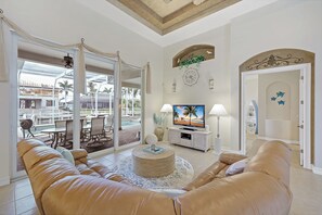 A living room with a leather sofa, a TV, and a view of a pool and outdoor furniture.