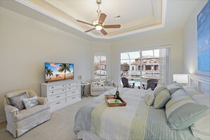 A bedroom with a bed, a TV, a ceiling fan, a window with a view, and a dresser.