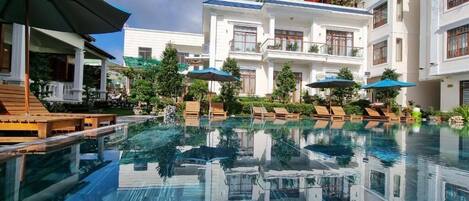 Una piscina con sillones de descanso y sombrillas, rodeada de edificios de varios pisos con balcones.