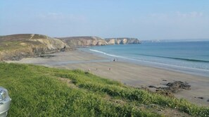 Un paisaje costero con una playa de arena, zonas de hierba y acantilados.