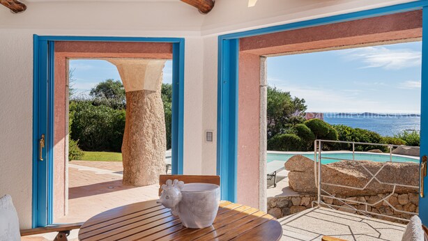 Une pièce avec une table en bois, un pilier en pierre et une vue sur une piscine et le paysage environnant.