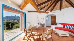 Une pièce spacieuse avec une table et des chaises en bois, un canapé rouge et une vue sur les montagnes par une grande fenêtre.