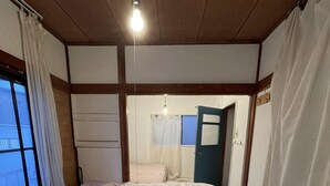 Un dormitori amb dos llits, una cadira de vimetes, una finestra amb cortines i una porta.