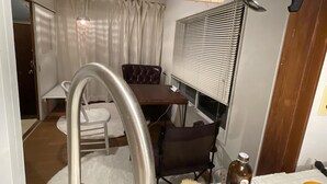 Cuina moderna amb un obrador d'acer inoxidable, zona de dinar amb taula i cadires, i finestra amb persianes.