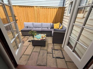 An outdoor patio area with a grey sofa, a wicker side table, and a potted plant. - 11 Crabbe Street, Aldeburgh (Aldeburgh)