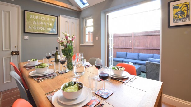 A dining area with a wooden table set for a meal, a vase with flowers, and a framed quote on the wall. - 11 Crabbe Street, Aldeburgh (Aldeburgh)