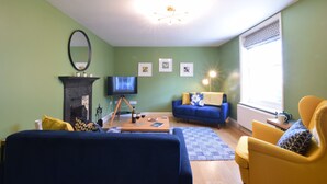 A living room with a blue sofa, a yellow armchair, a coffee table, and a fireplace with a TV. - 11 Crabbe Street, Aldeburgh (Aldeburgh)