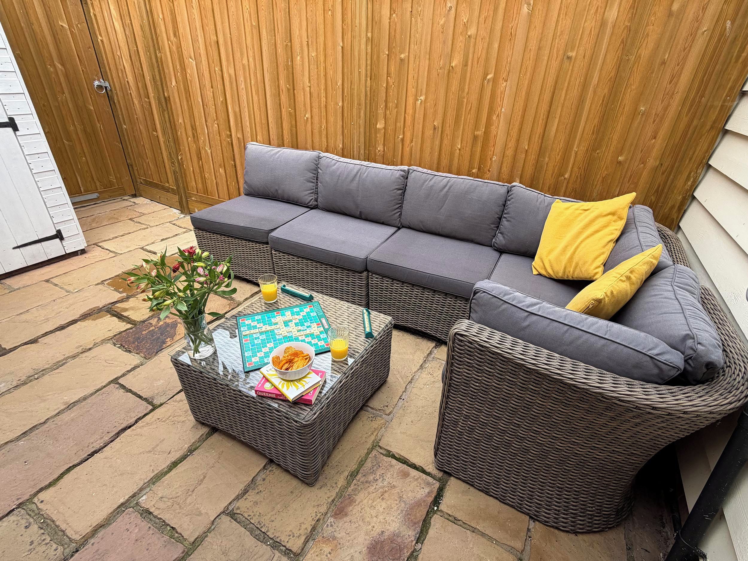 A grey sectional sofa with yellow cushions, a wicker coffee table with a crossword puzzle, a bowl of croissants, and a glass of orange juice.