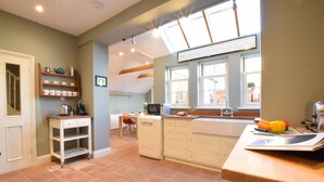 A kitchen with a white refrigerator, a microwave, and a sink. There are shelves with kitchenware and a window above the sink. - 11 Crabbe Street, Aldeburgh (Aldeburgh)
