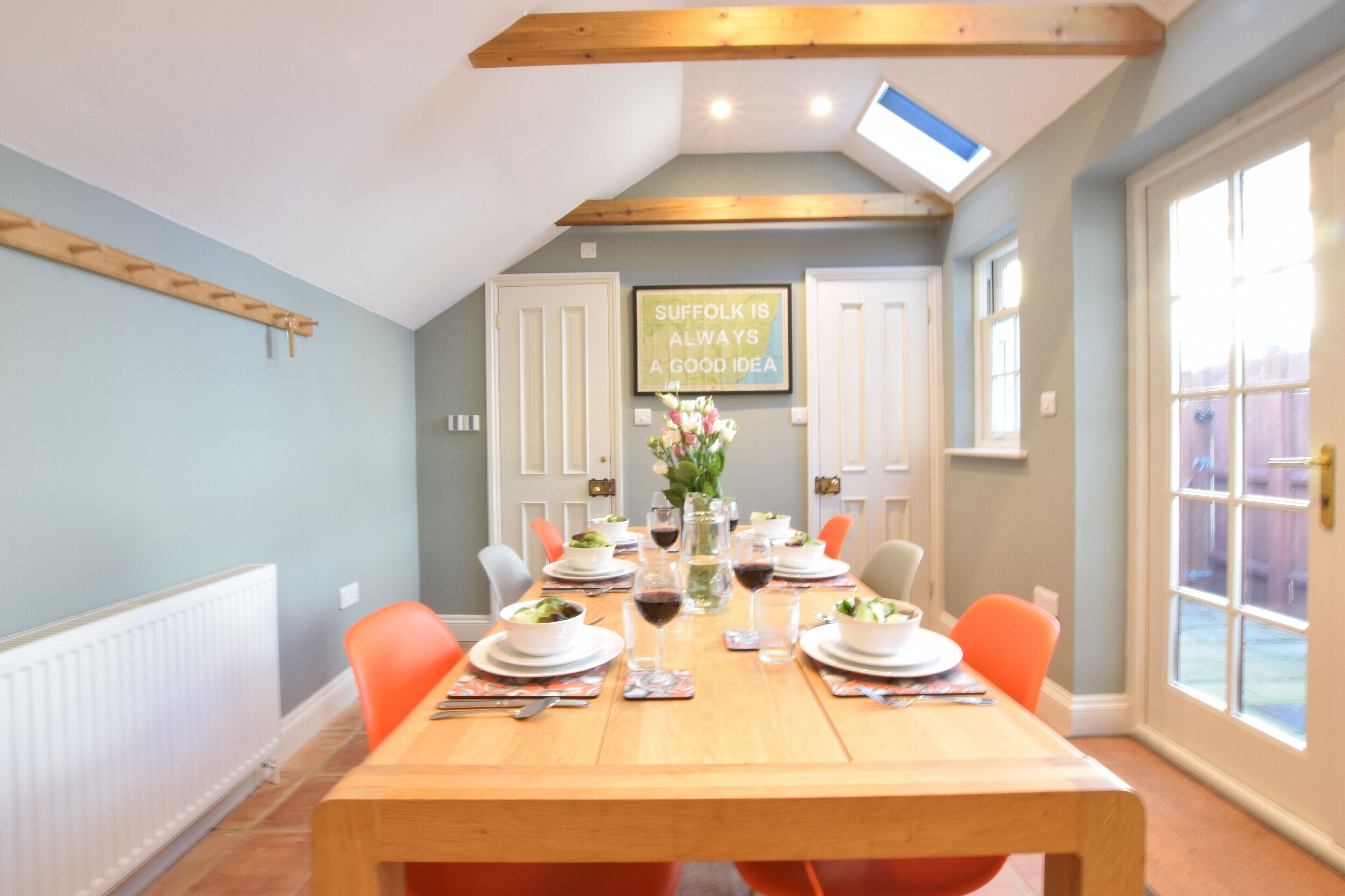 A dining area with a wooden table set for four, surrounded by orange chairs.