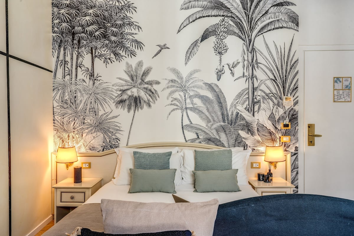 A bedroom with a bed, two nightstands, and a wall mural of tropical foliage.