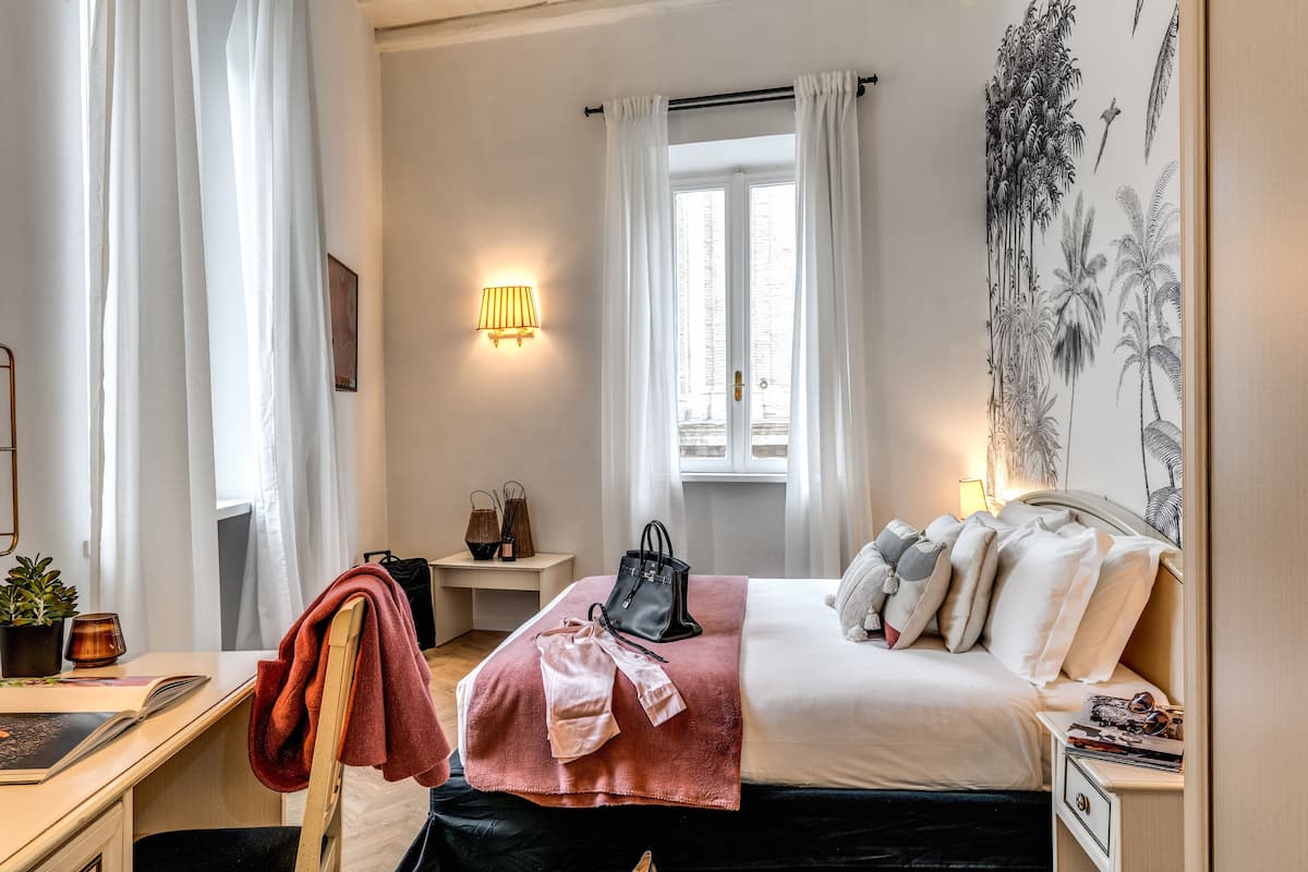 A hotel room with a bed, bedside table, lamp, and a window with curtains.