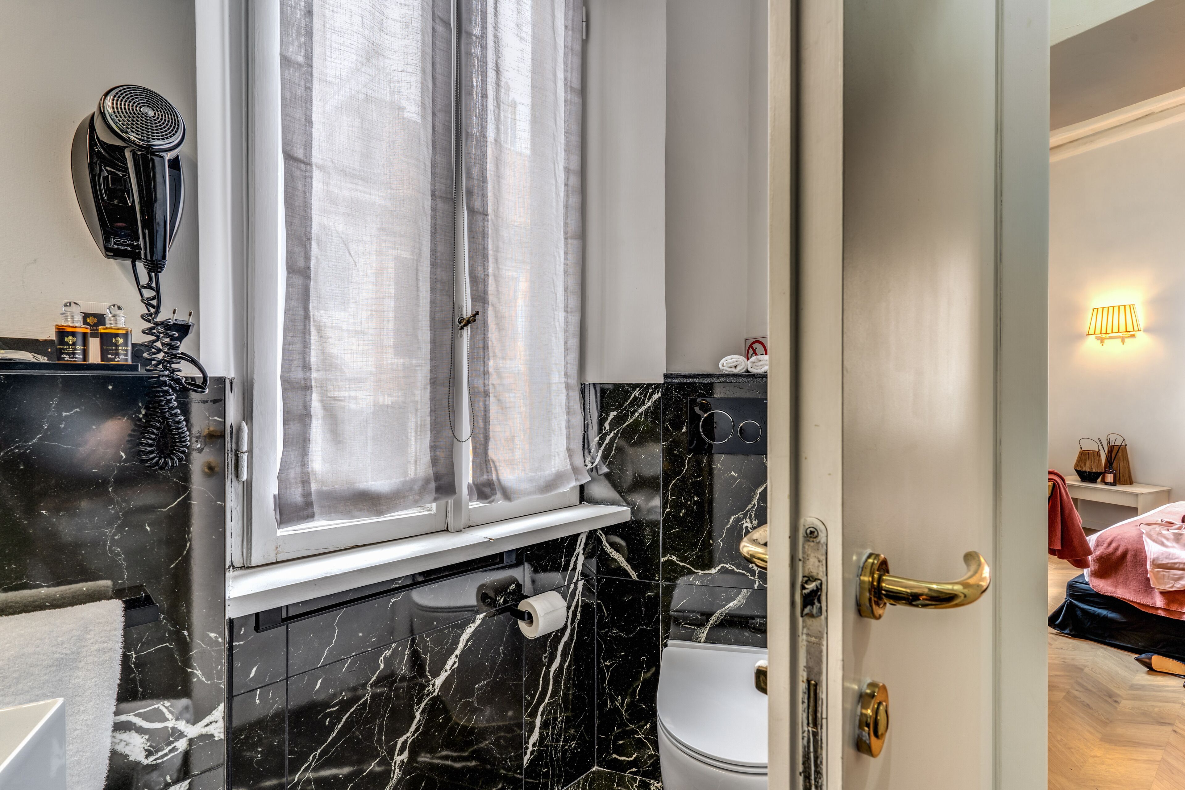 A bathroom with a black marble sink, a hairdryer on the wall, and a toilet with a gold door handle.