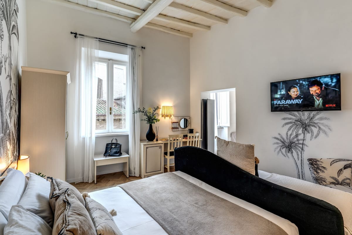 A bedroom with a bed, a desk, a TV, and a window with curtains.
