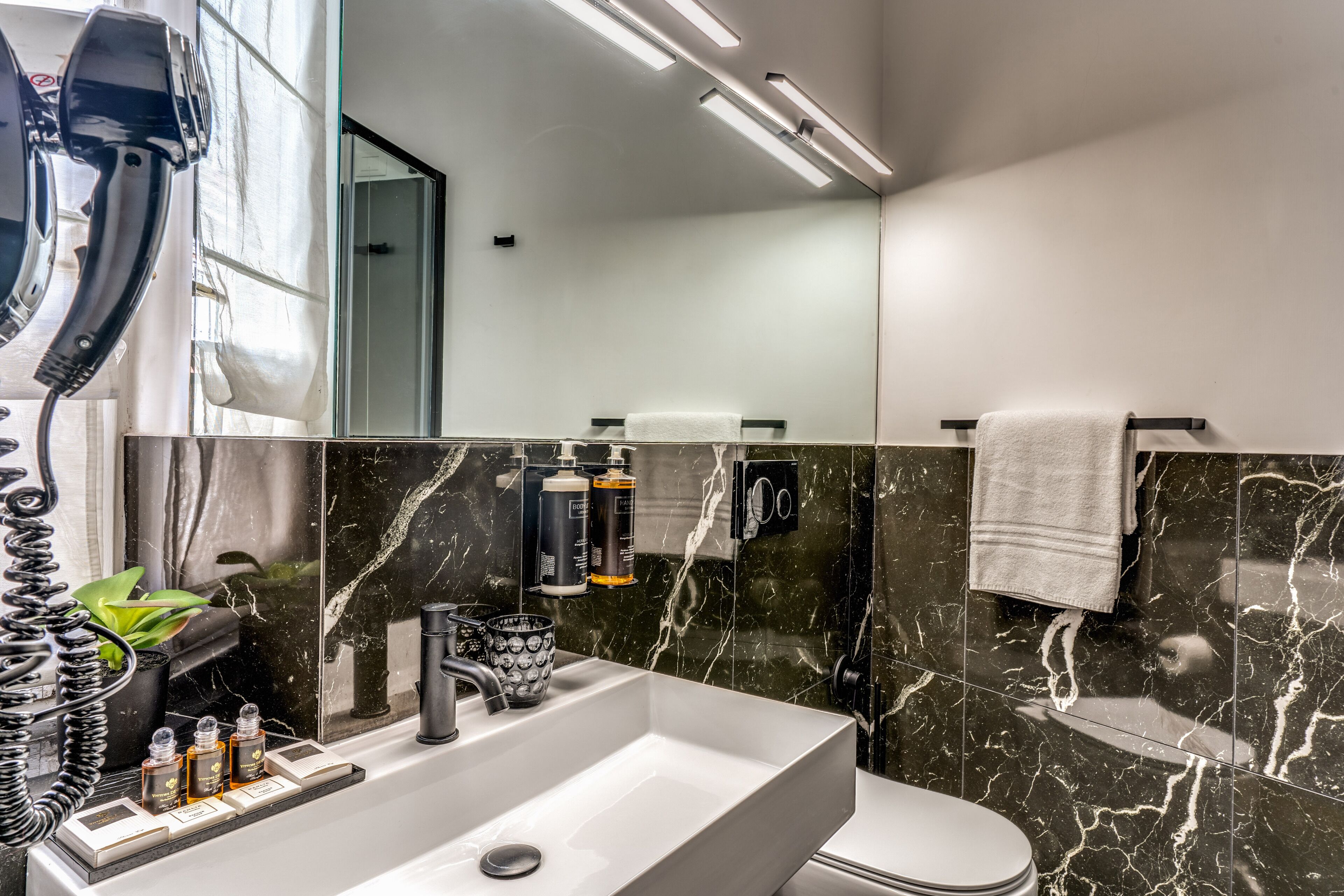 A modern bathroom with a white sink, black marble tiles, a towel rack, and a toilet.