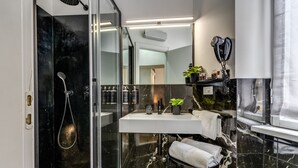 A modern bathroom with a glass-enclosed shower, a white sink, and a hairdryer mounted on the wall. - Baboon Room (Rome)