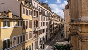 A street view of a historic European town with multi-story buildings, a cobblestone street, and pedestrians. - Baboon Room (Rome)