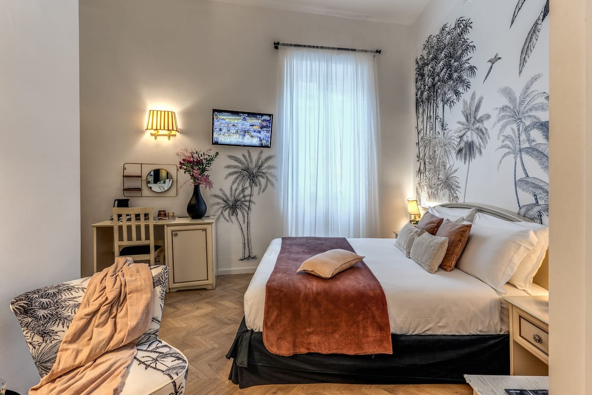 A hotel room with a bed, a desk, a chair, a TV, and a wall with a tropical mural.