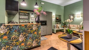 A modern kitchen with a central island, a dining area with a round table, and a living space with a sofa and decorative plants. - Baboon Room (Rome)