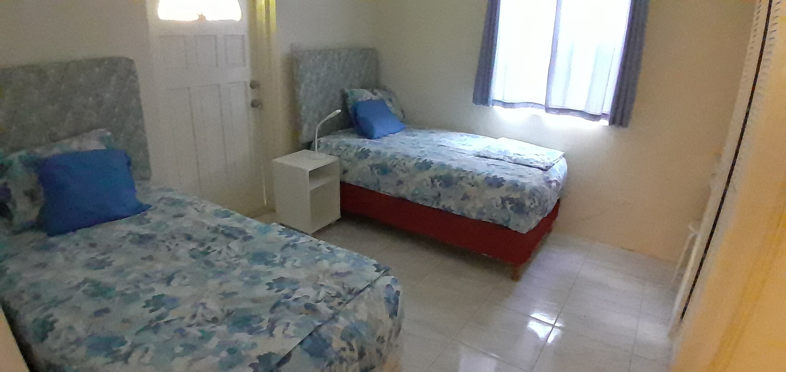 A small, clean room with two beds, a nightstand, and a window with curtains.