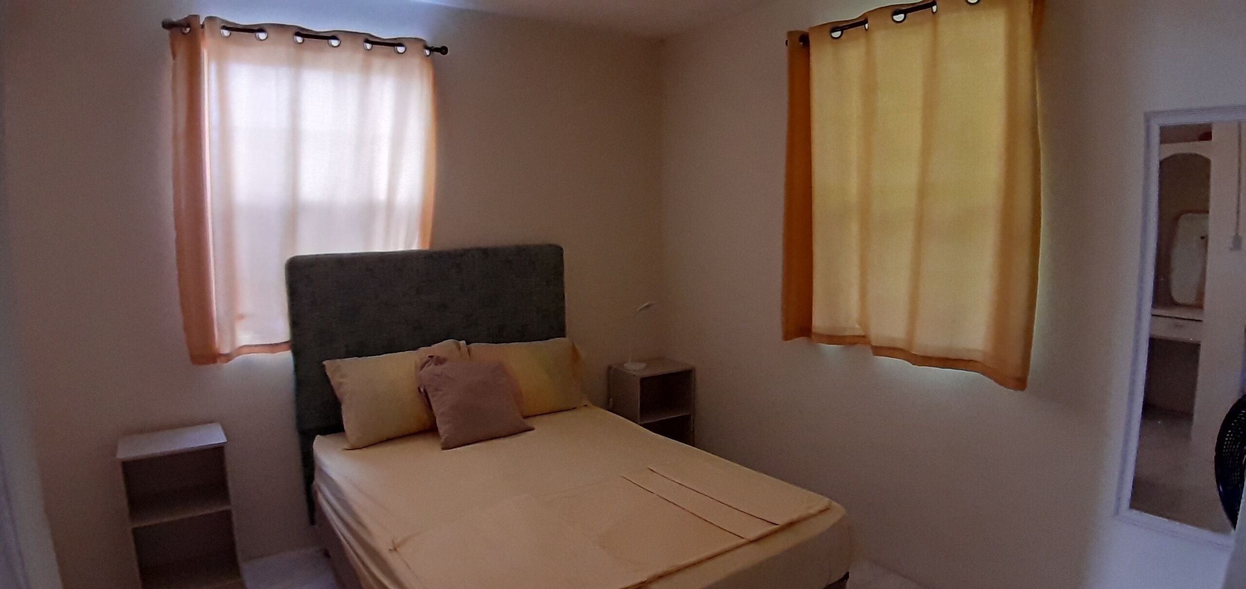 A small, single-bed room with a plain headboard, two bedside tables, and a window with curtains.