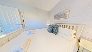 A neatly made bed with white linens, a headboard, and a nightstand with a lamp.