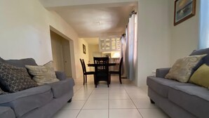 A living room with two grey sofas, a dining table with chairs, and a kitchen area in the background. - Oistins 2 Bed Apartment with AC Near Miami Beach & Oistins. (Christ Church)