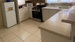 A compact kitchen with white cabinets, a refrigerator, a microwave, an oven, and a sink. - Oistins 2 Bed Apartment with AC Near Miami Beach & Oistins. (Christ Church)