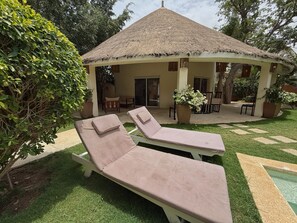 A thatched-roof gazebo with two lounge chairs, a potted plant, and a patio area with a patterned floor. - Villa N°301 Résidence du Port (Saly)