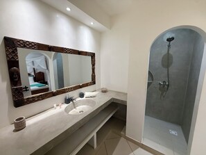 A bathroom with a large mirror, a sink, a shower, and a bench.