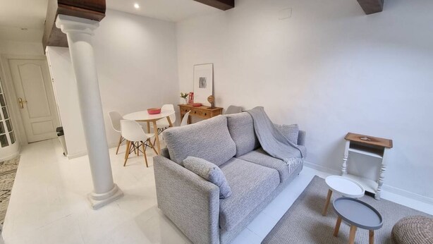 Ein Wohnzimmer mit einem grauen Sofa, einem kleinen runden Tisch und einem weißen Stuhl.