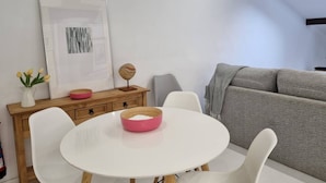 Ein Essbereich mit einem weißen Tisch, Stühlen, einer Holzkommode und einem grauen Sofa.
