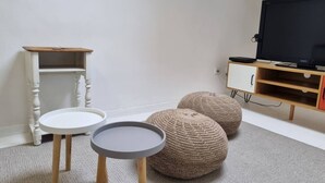 Ein Zimmer mit weißer Wand, einem Holzschrank, einem Fernseher und zwei runden Hocker.