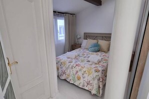 Un dormitorio con cama, mesita de noche y ventana con cortinas.