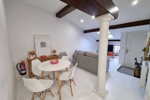 Una sala de estar moderna con un sofá blanco, una mesa de comedor con sillas, un extintor y un cuadro en la pared.
