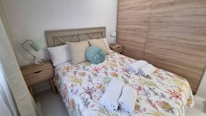 Ein Schlafzimmer mit einem Holz-Kopfteil, einer blumigen Bettdecke, zwei Kissen, einem Nachttisch mit Lampe und einem Holzschrank.