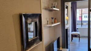 A hotel room with a mirror, a flat-screen TV, a small table, a chair, and a view of the outside.